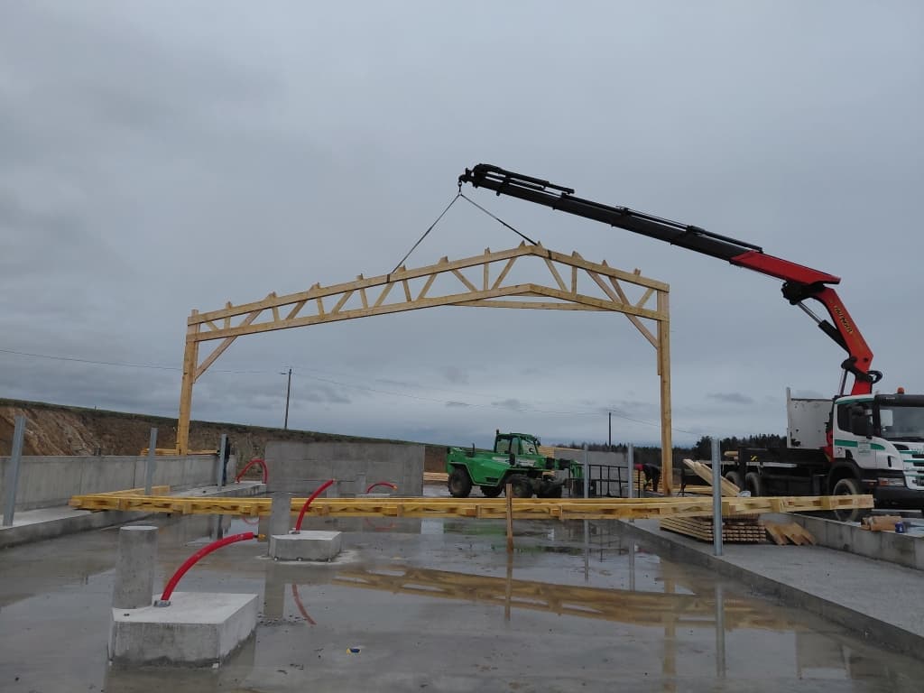 Camion grue posant une ferme de charpente bois sur un bâtiment agricole à Jurine